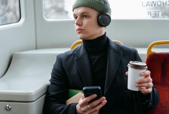 Junger Mann im Zug, der einen Kaffee im Becher und sein Smartphone in der Hand hat, dabei aus dem Fenster guckt